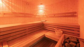A wooden sauna with benches, a bench, a bucket, and a container of stones.