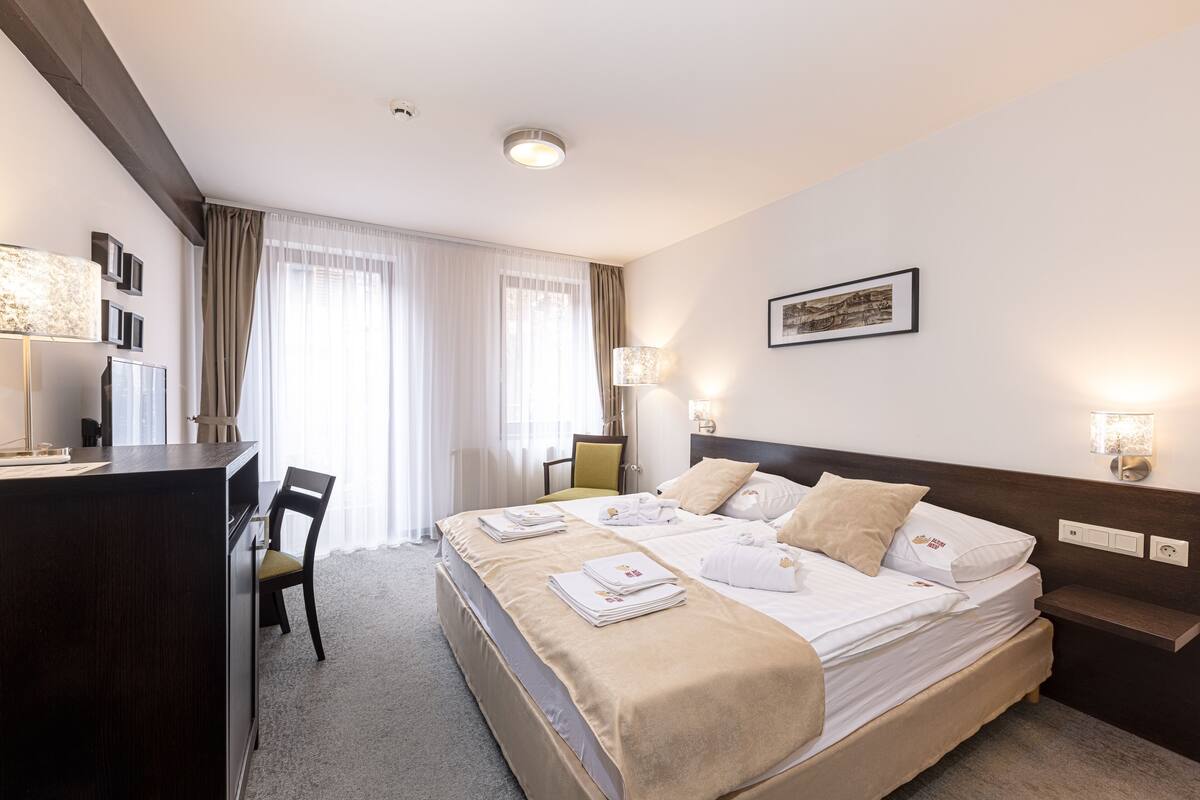 Une chambre d’hôtel avec un grand lit, un bureau avec une chaise, une table de chevet et une fenêtre avec des rideaux.