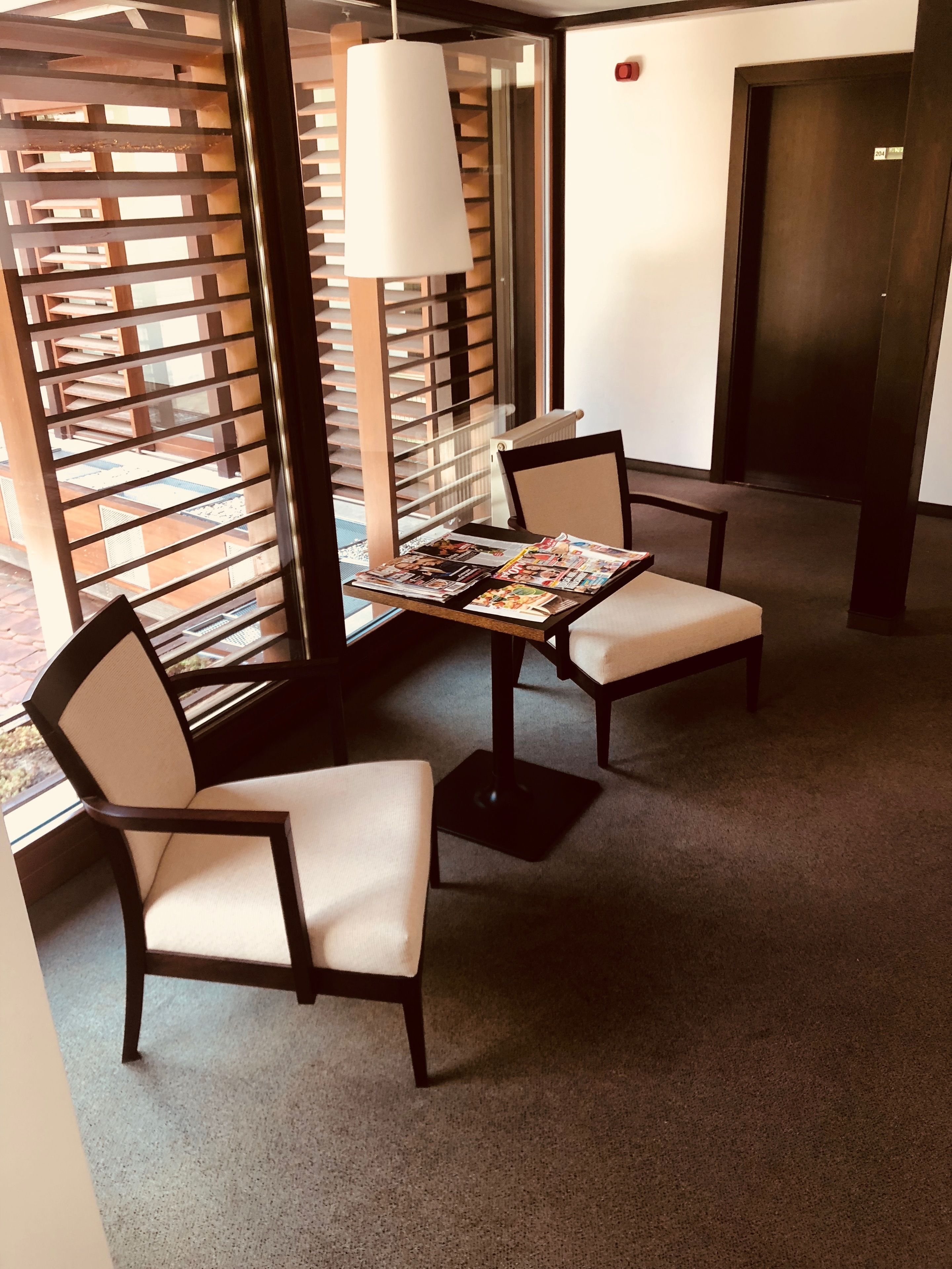 A hotel lobby with a seating area featuring a table with magazines, two chairs, and a hanging light fixture.