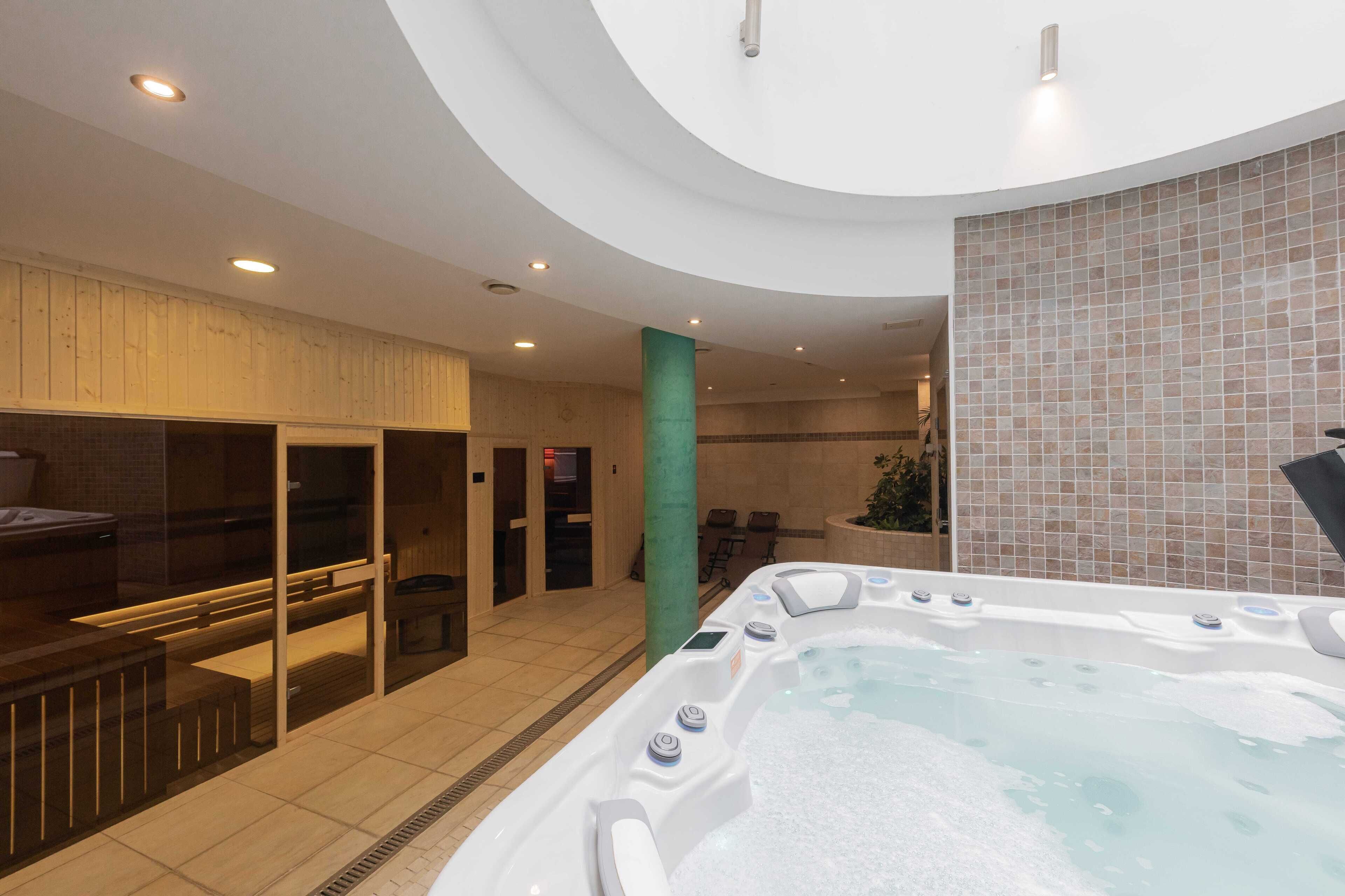 A modern spa area with a hot tub, wooden seating, and a tiled wall.