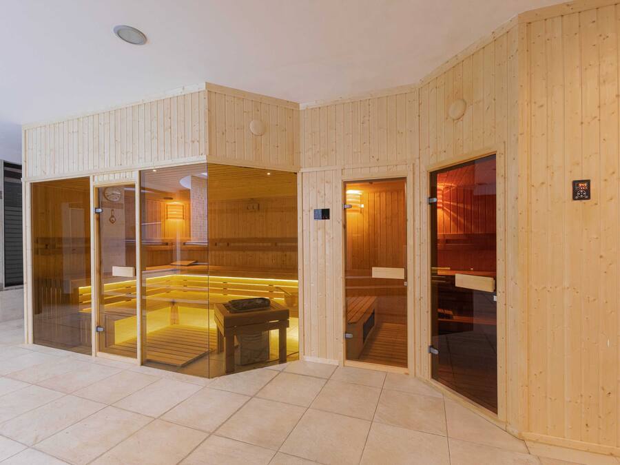 A sauna with wooden walls and glass doors, a bench, and a table with a bowl.