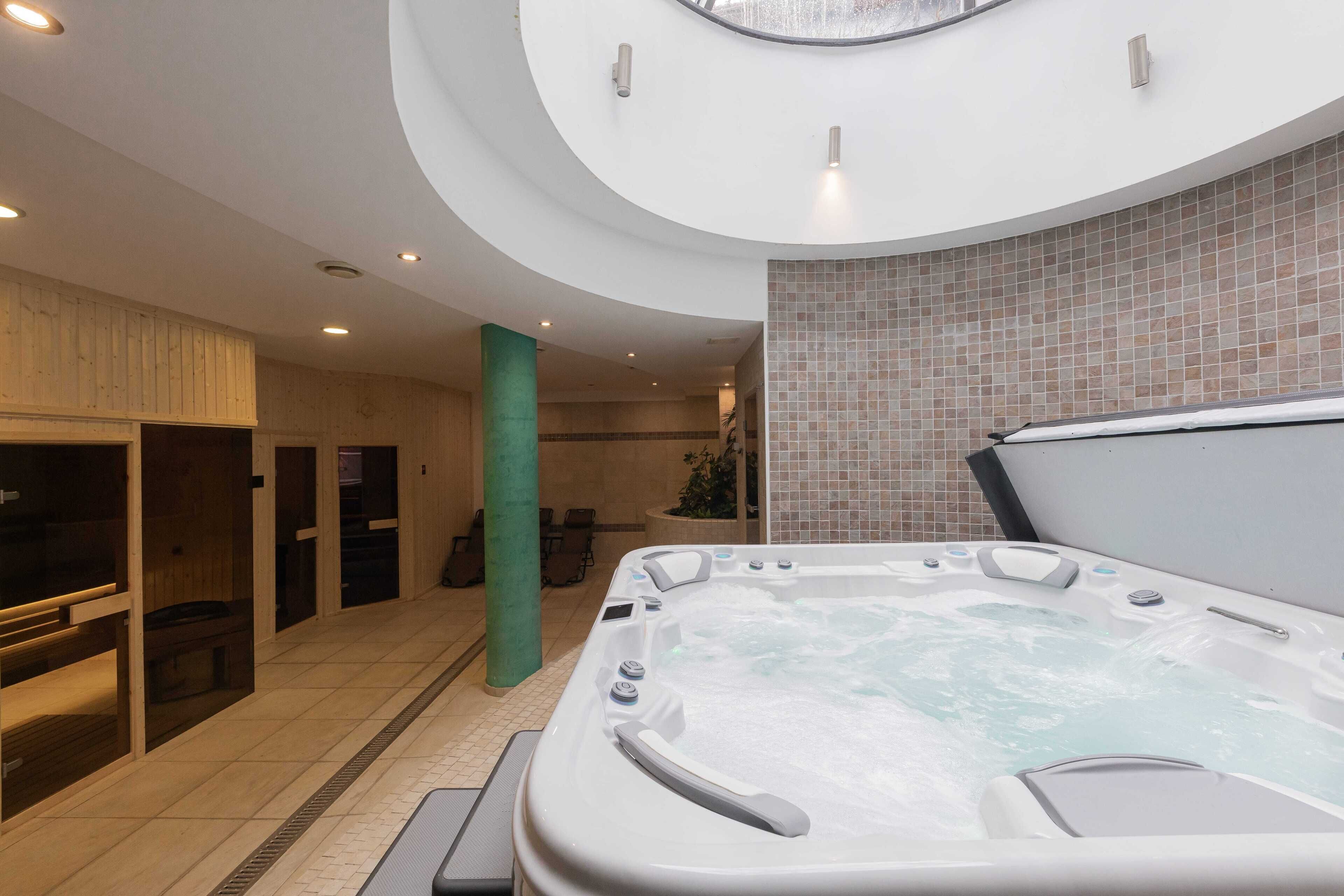 A modern spa area with a hot tub, wooden cabinets, and a tiled wall.