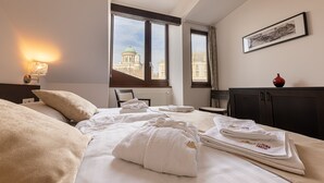 Une chambre d’hôtel avec un lit, des serviettes, une lampe, une fenêtre donnant sur un immeuble et un tableau encadré au mur.