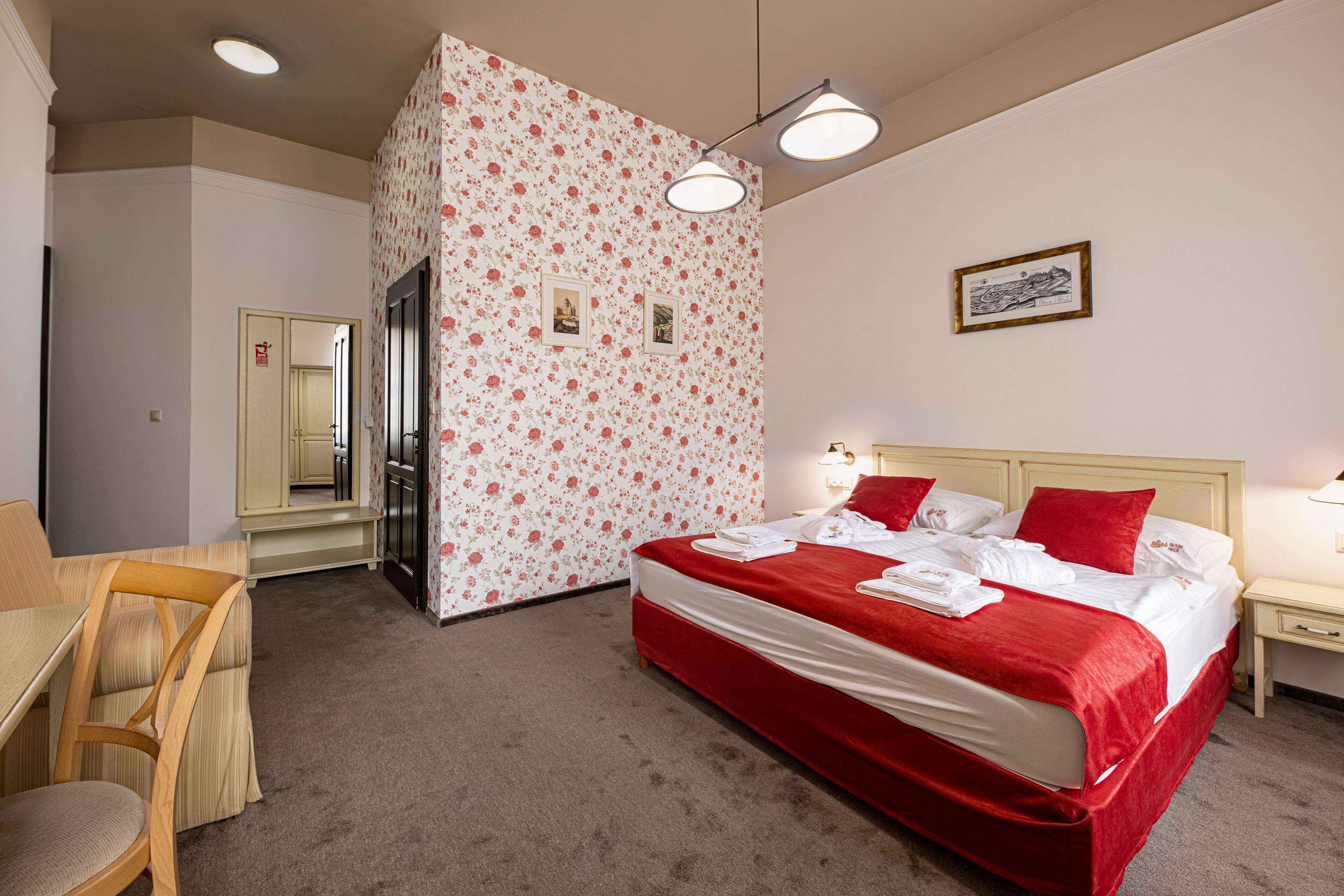 A hotel room with a bed, a desk, and a chair. There is a mirror and a picture on the wall.