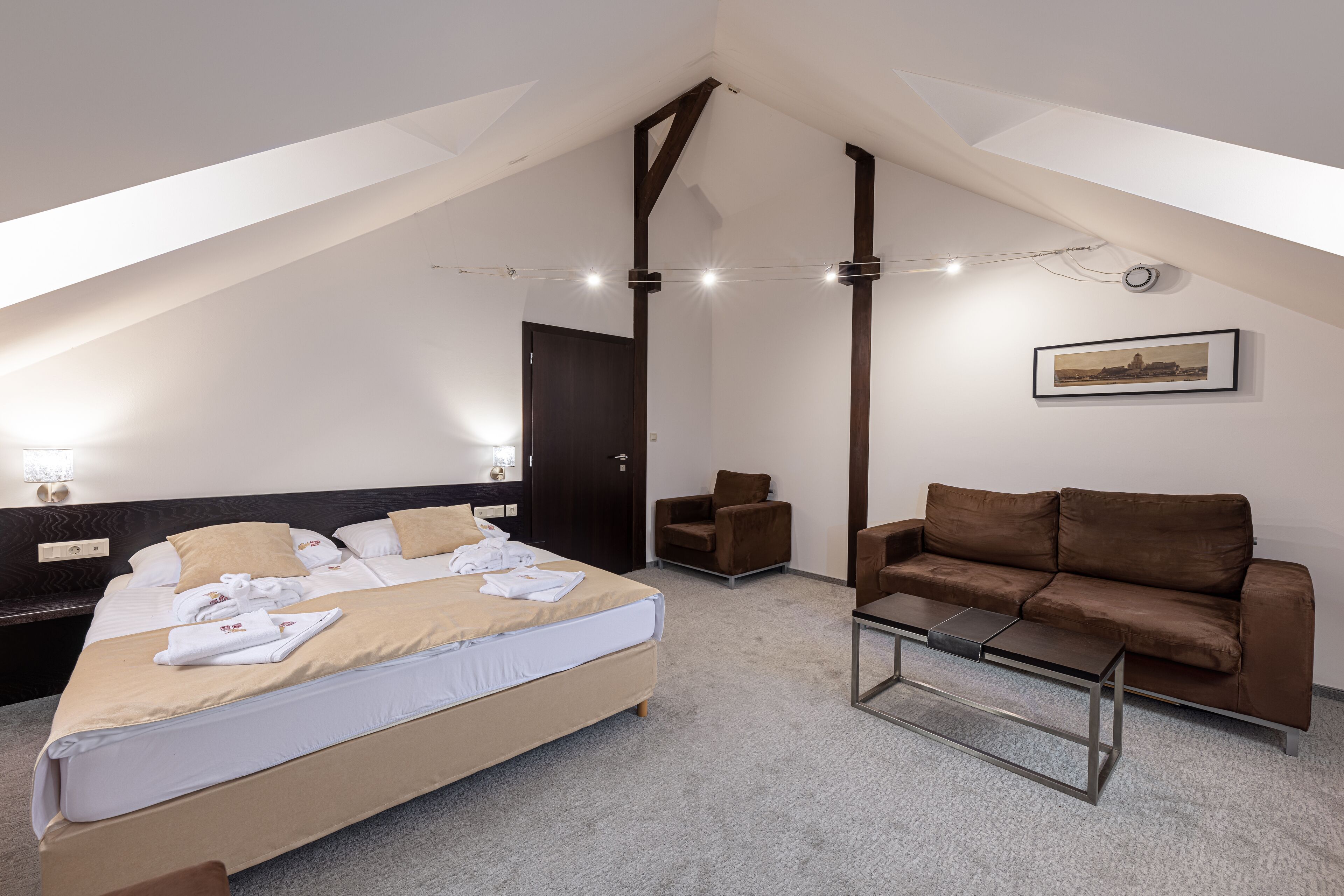 A modern hotel room with a large bed, a brown sofa, a small table, and a framed picture on the wall.