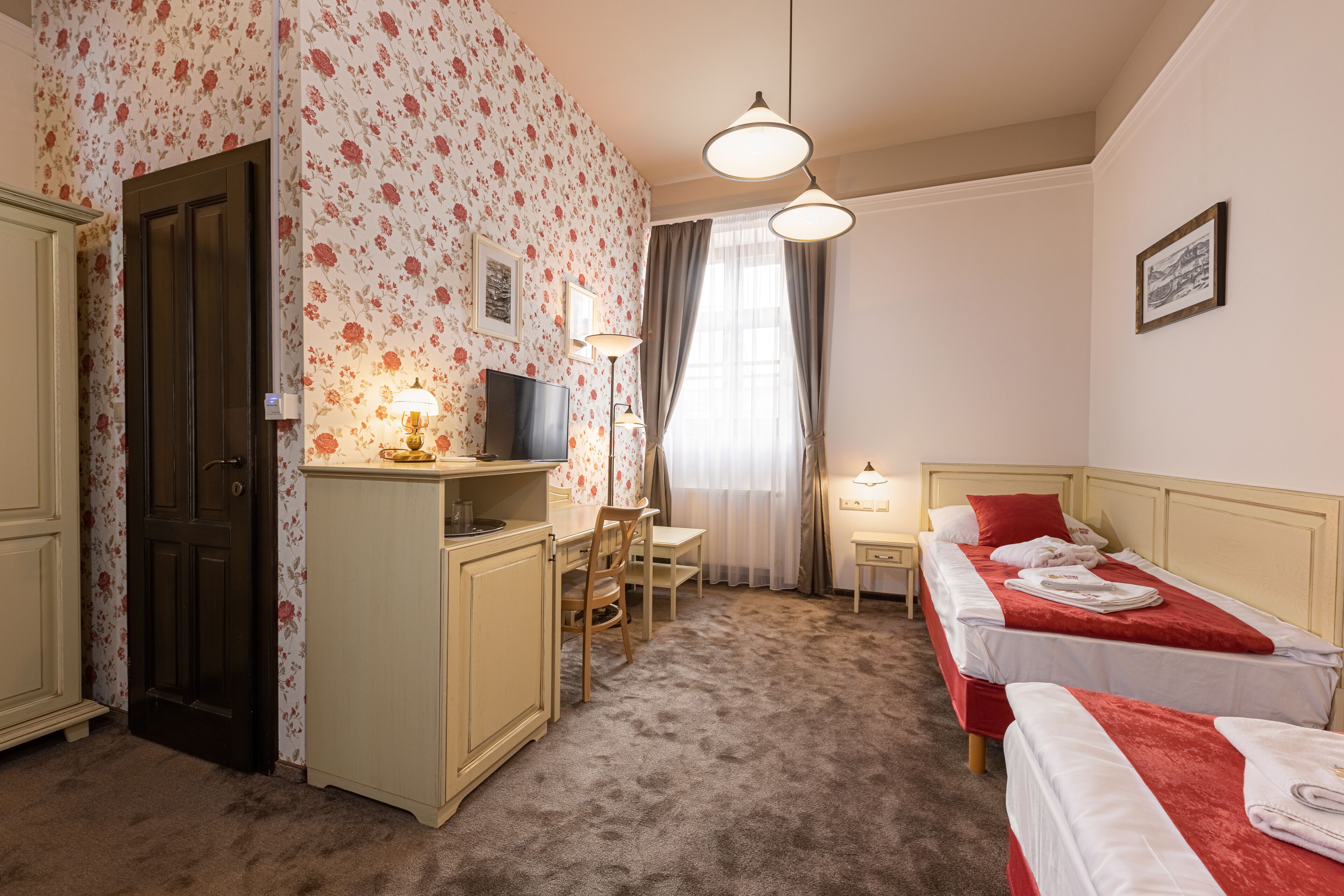 A room with two beds, a desk, a chair, a TV, and a window with curtains.