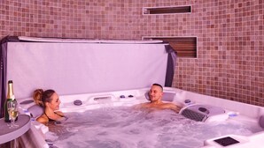 Un bain à remous pour deux personnes, une bouteille de champagne et une petite table avec une bouteille.