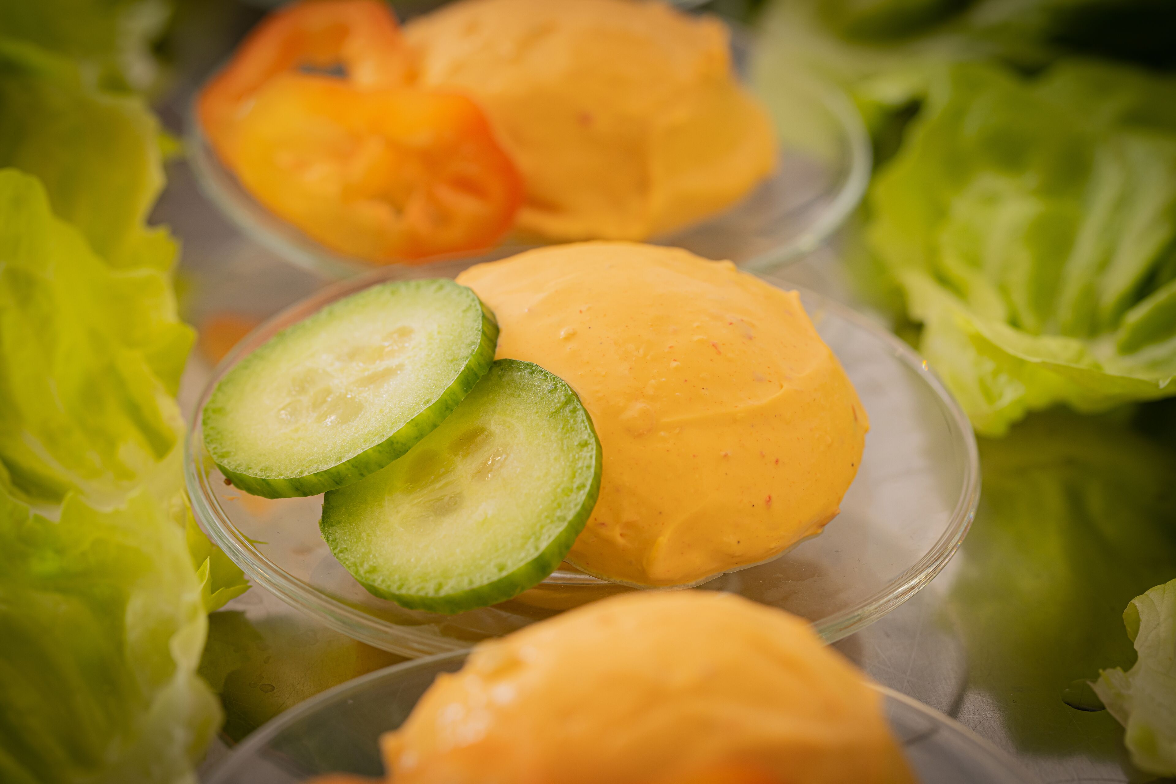 A clear glass container with a yellow substance, possibly a dessert or food item, surrounded by green lettuce leaves.