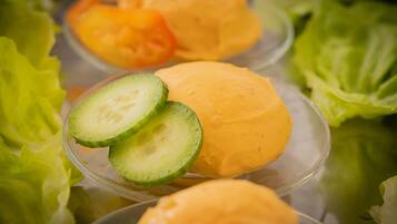 A clear glass container with a yellow substance, possibly a dessert or food item, surrounded by green lettuce leaves.