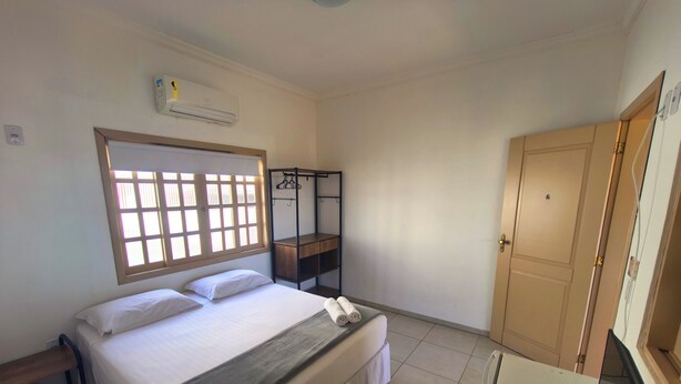 A bedroom with a bed, a desk, a wardrobe, and a window with blinds. - Pousada Solar do Jabaquara (Paraty)