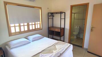 A bedroom with a bed, a wooden wardrobe, a bathroom with a toilet and sink, and an air conditioning unit.