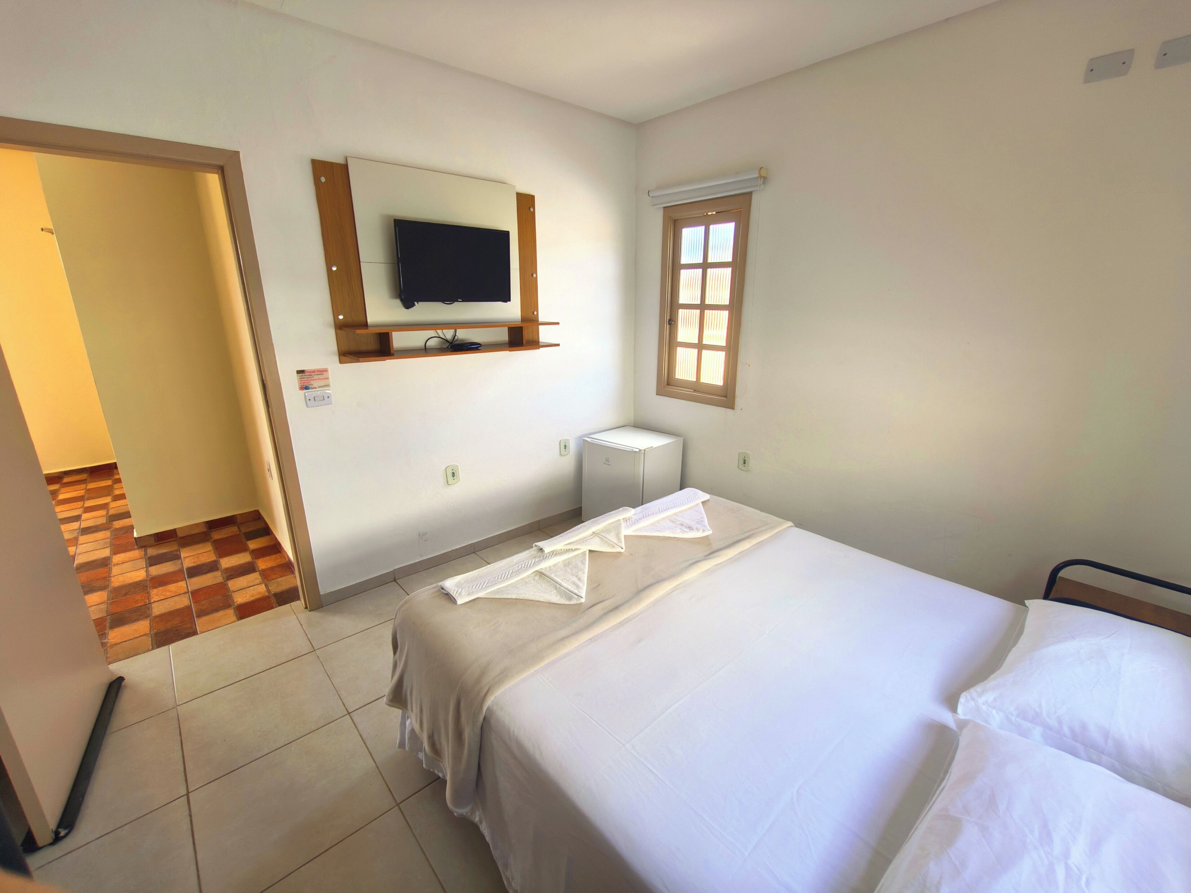 A hotel room with a bed, a television mounted on the wall, a window, and a radiator.