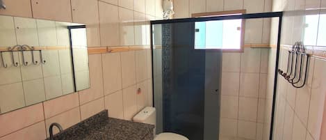 A bathroom with a granite countertop sink, a toilet, a glass shower enclosure, and a mirror.
