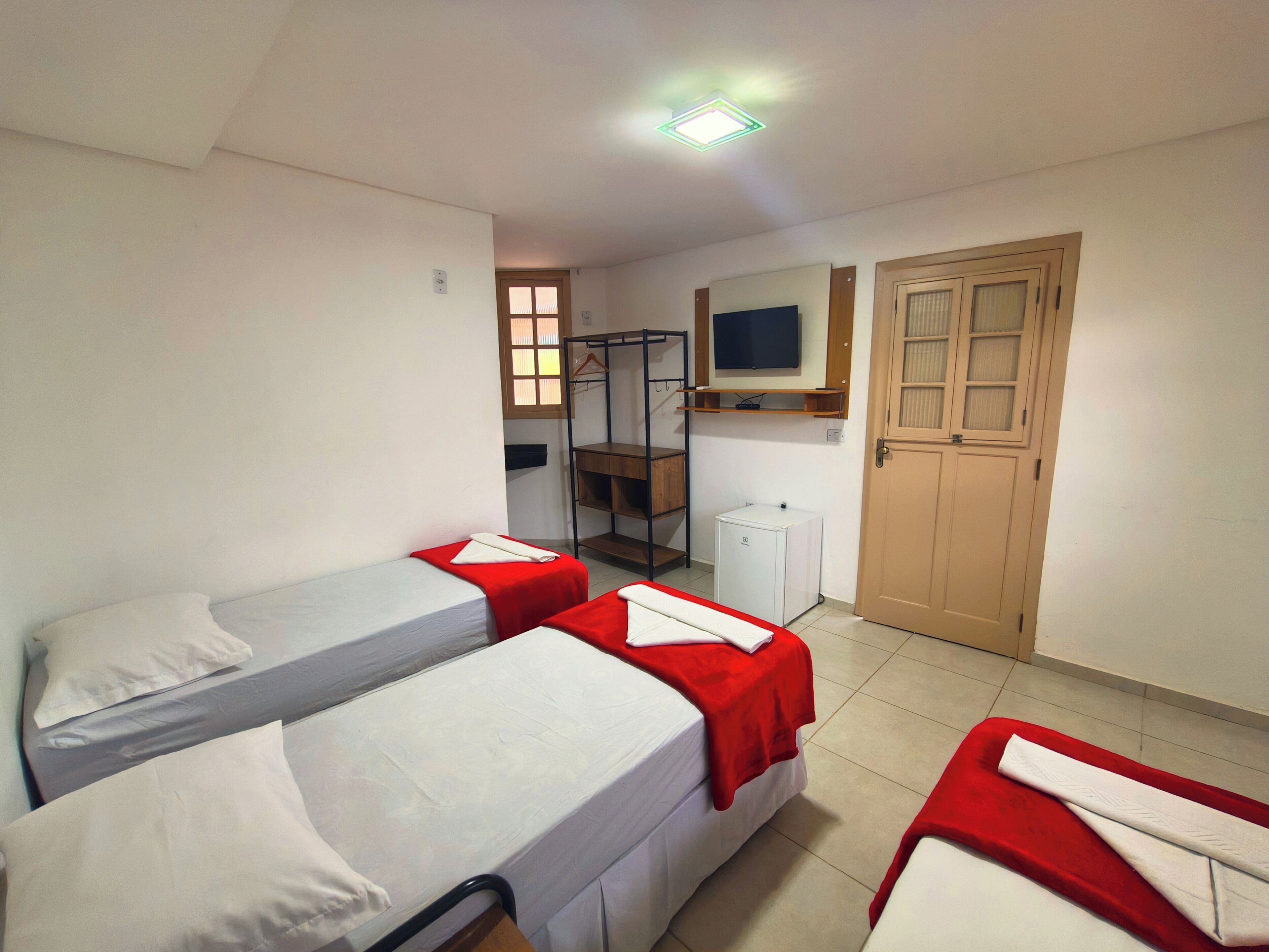 Une chambre de dortoir avec deux lits simples, un petit bureau, une télévision et une armoire.