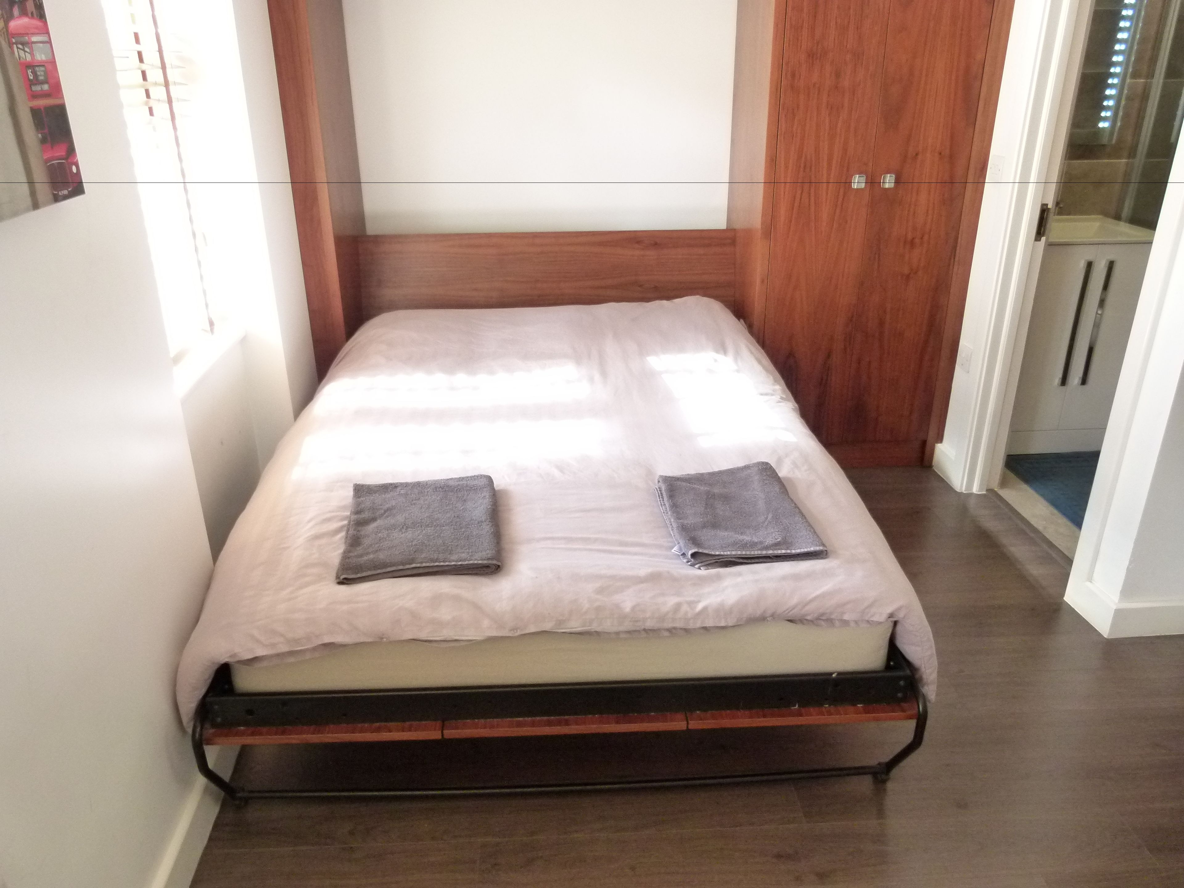 Una cama individual con cabecera de madera, una colcha gris y una almohada gris.