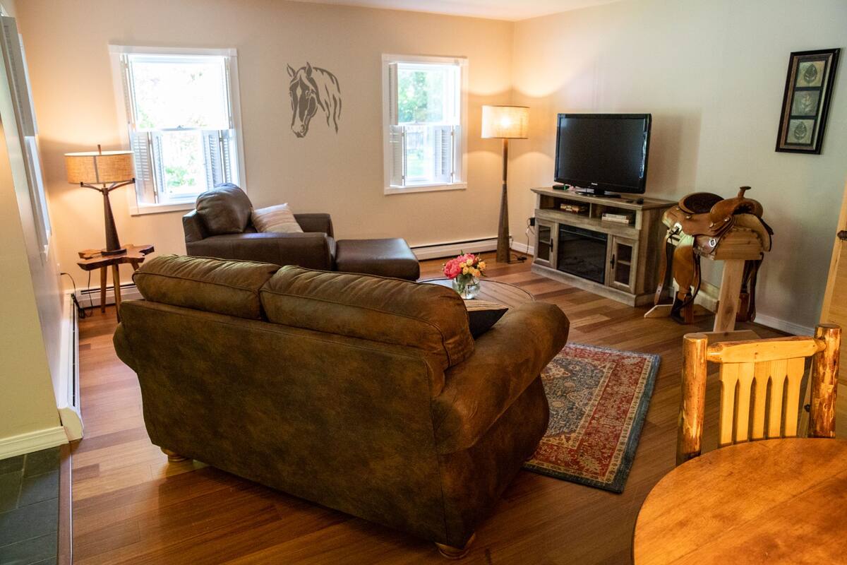 A living room with a brown sofa, a television, a fireplace, and a horse statue.