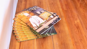 Une table en bois sur laquelle se trouve une pile de magazines et un vase rempli de fleurs roses.