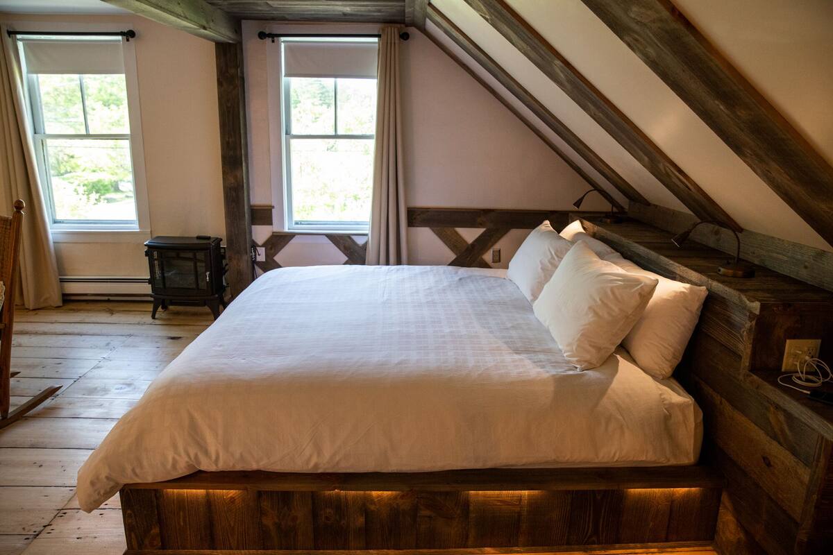 A bedroom with a wooden bed frame, white bedding, and a sloped ceiling.