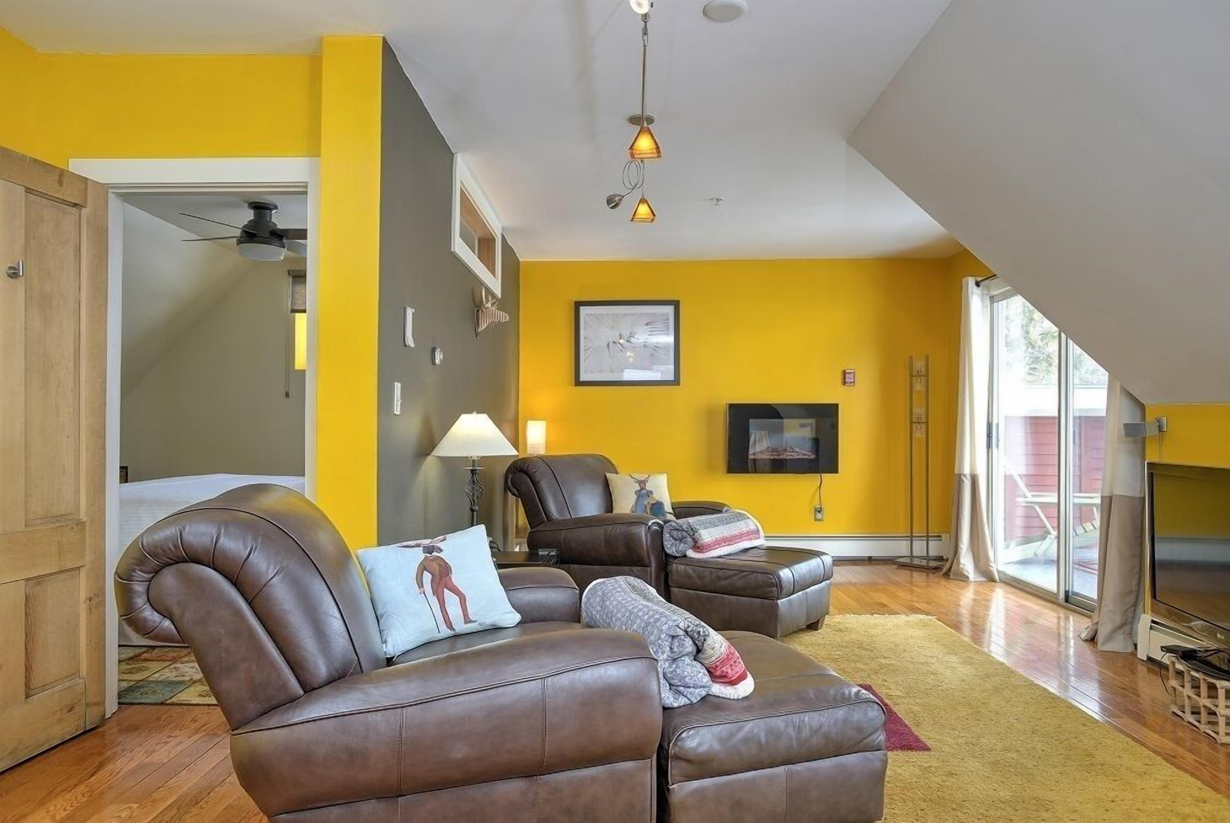 Ein modernes Wohnzimmer mit Sofa, Sessel, Hocker, Fernseher und Deckenventilator.