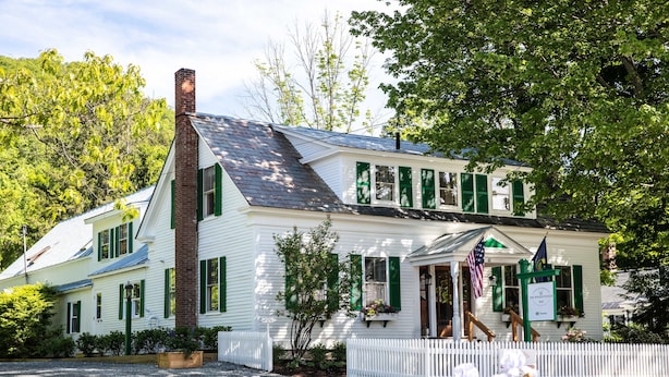 Un bâtiment blanc avec des volets verts, une cheminée en briques et une clôture en piquets.