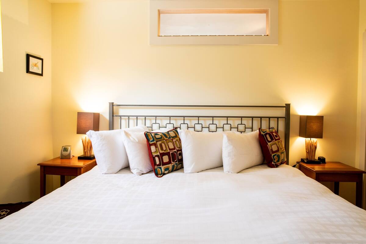 A neatly made bed with white bedding and decorative pillows, flanked by two bedside tables with lamps, in a room with a simple, clean design.