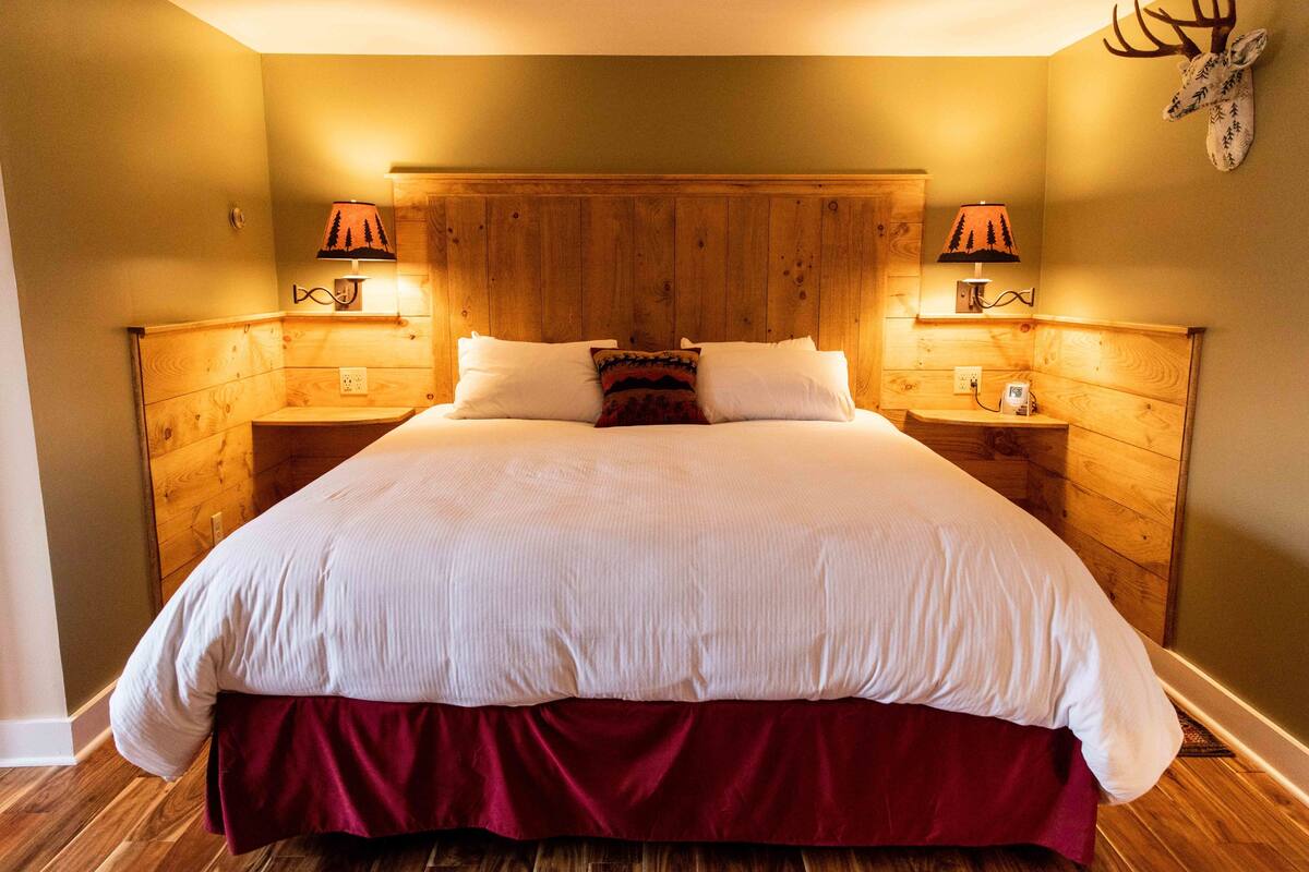 A large bed with a wooden headboard, two bedside lamps, and a decorative headpiece on the wall.