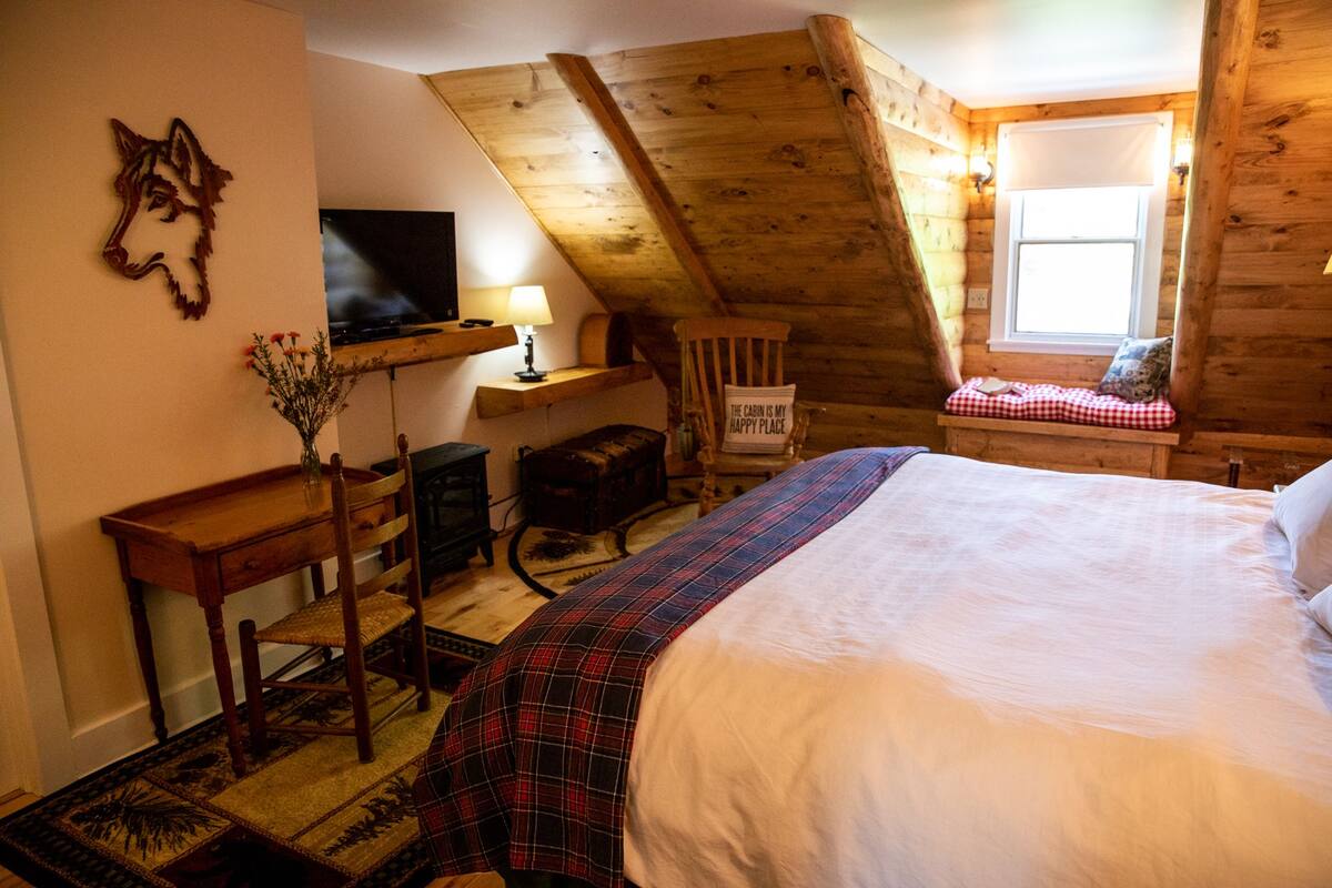 A cozy cabin room with a bed, a desk, a television, and a window.