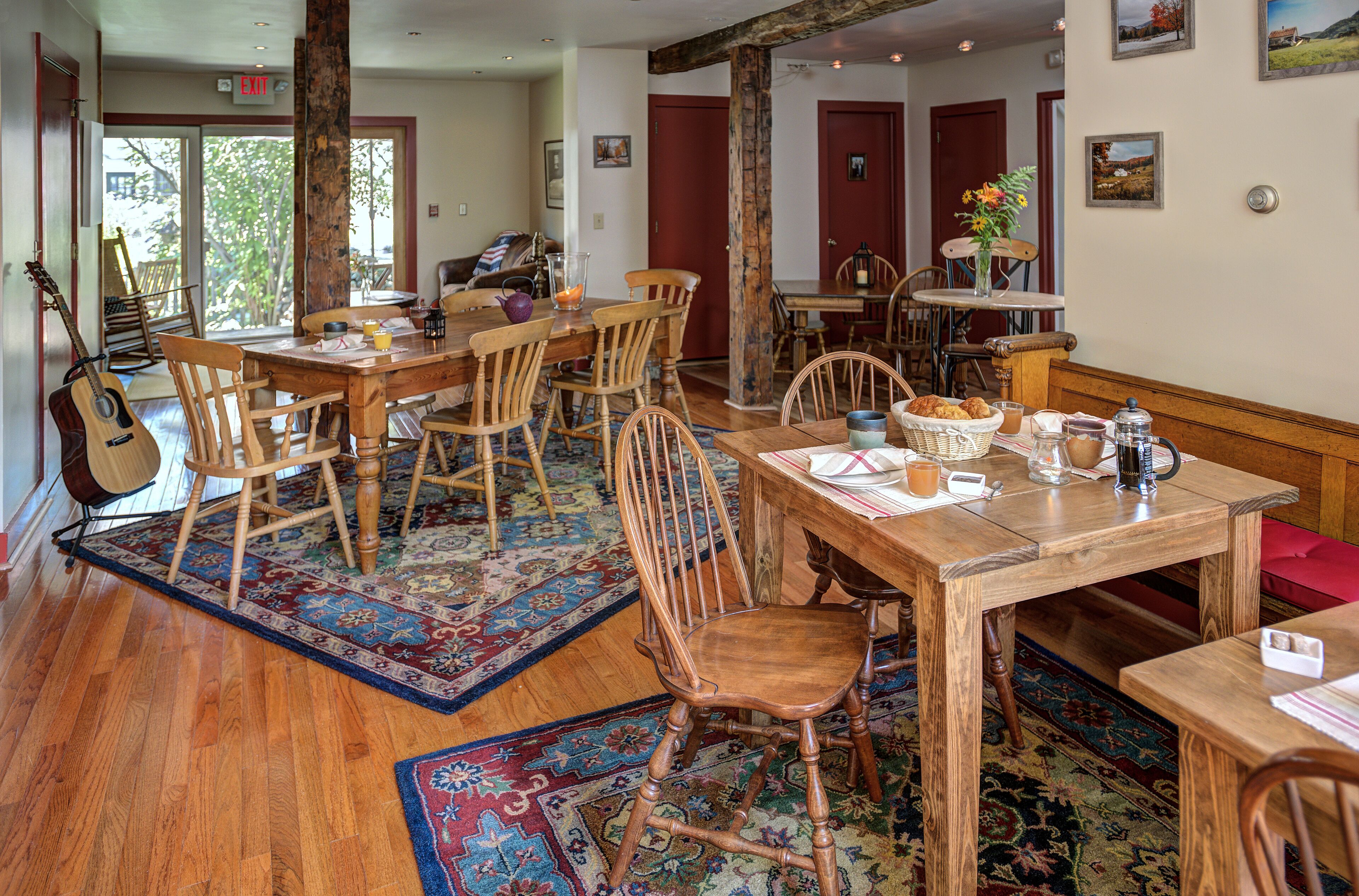A dining area with wooden tables and chairs, a guitar, and a rug.