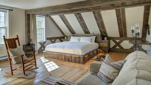 Une chambre avec un plafond en bois, un grand lit, un fauteuil à bascule et un canapé.