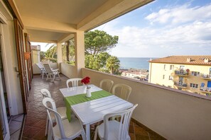 Ein Balkon mit Tisch und Stühlen, mit Blick auf eine Küstenlandschaft mit Gebäuden und Bäumen.