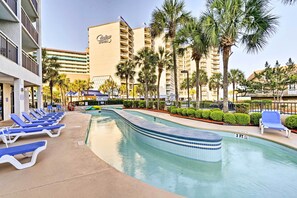 A hotel pool area with blue lounge chairs, a clear pool, and palm trees. - Pools, Patio & Stunning Views: Myrtle Beach Oasis (Myrtle Beach)