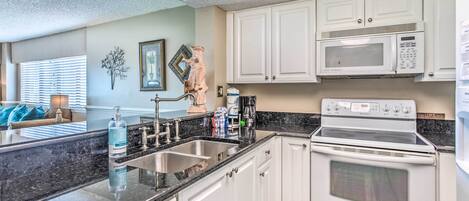 A kitchen with white cabinets, a stainless steel sink, a built-in oven, and a microwave.