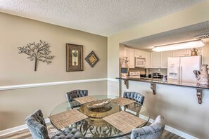 A dining area with a glass table surrounded by four chairs, a decorative metal tree, and framed artwork on the wall. - Pools, Patio & Stunning Views: Myrtle Beach Oasis (Myrtle Beach)