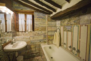 A bathroom with a tiled wall, a sink, a bathtub, and a window with curtains. - Appartamento La Scaletta (Capoliveri)