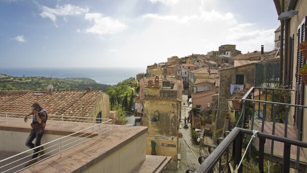 A view of a coastal town with terracotta-roofed buildings, a person on a rooftop, and a clear sky. - Appartamento La Scaletta (Capoliveri)