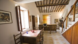 A dining area with a wooden table and chairs, a TV, and a staircase leading to another level. - Appartamento La Scaletta (Capoliveri)