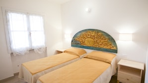 Ein Zimmer mit zwei Einzelbetten, einem Fenster mit leichtem Vorhang, einem Wandbild einer Sonne und einem kleinen Nachttisch aus Holz.