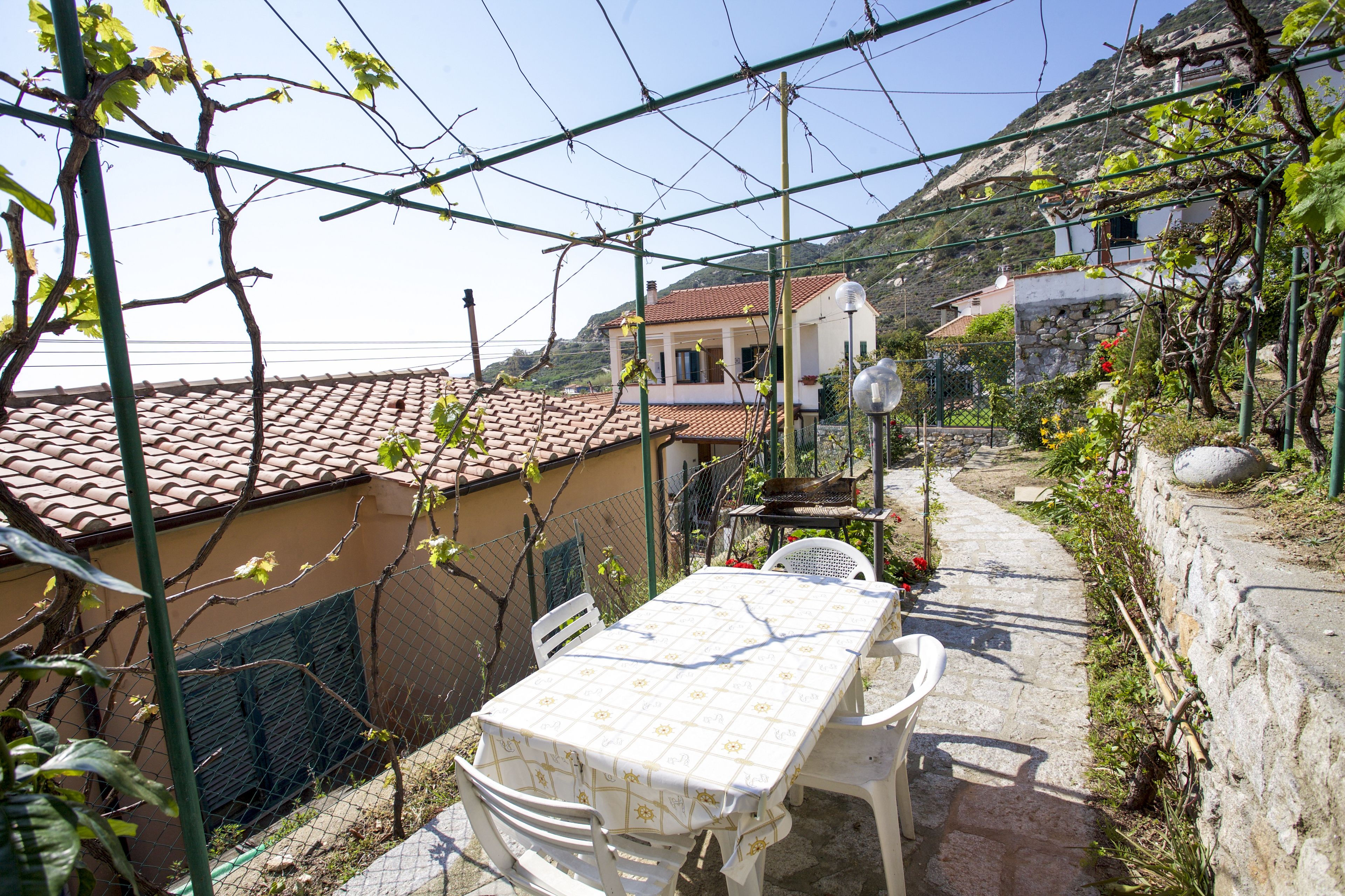 Zona exterior coberta amb taula i cadires, envoltada per una tanca de filferro i plantes.