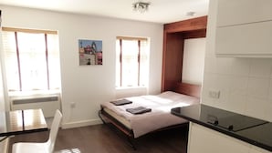 A compact bedroom with a bed, a small desk, and a kitchenette. - SS Property Hub - City of London Studio Apartment 12 (London)