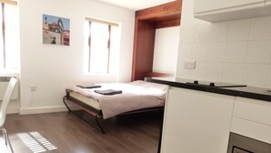 A compact room with a bed, a small kitchenette, and a window with curtains. - SS Property Hub - City of London Studio Apartment 12 (London)