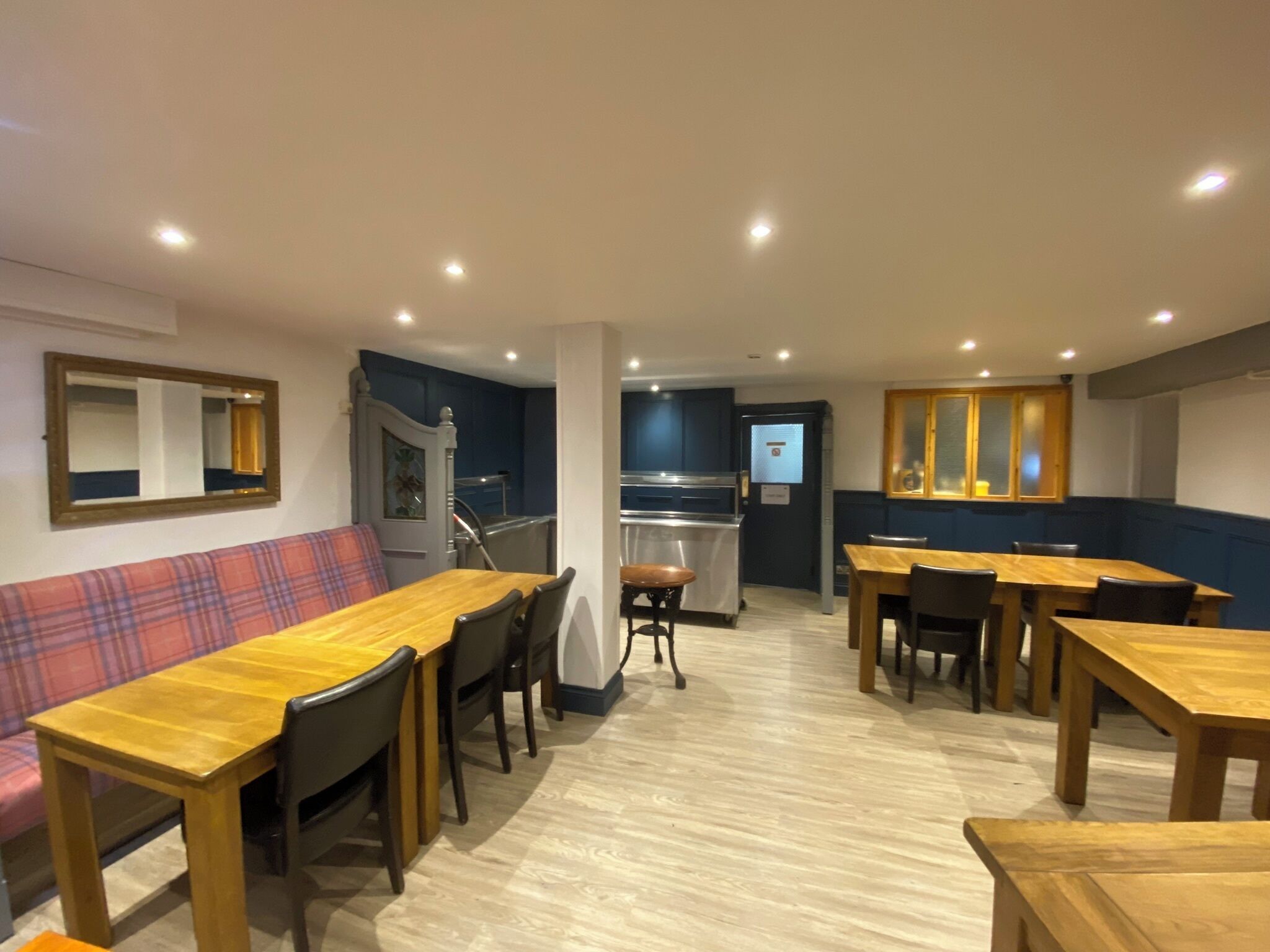 Un espace repas avec des tables et des chaises en bois, un canapé et un coin cuisine équipé d’un réfrigérateur et d’une cuisinière.