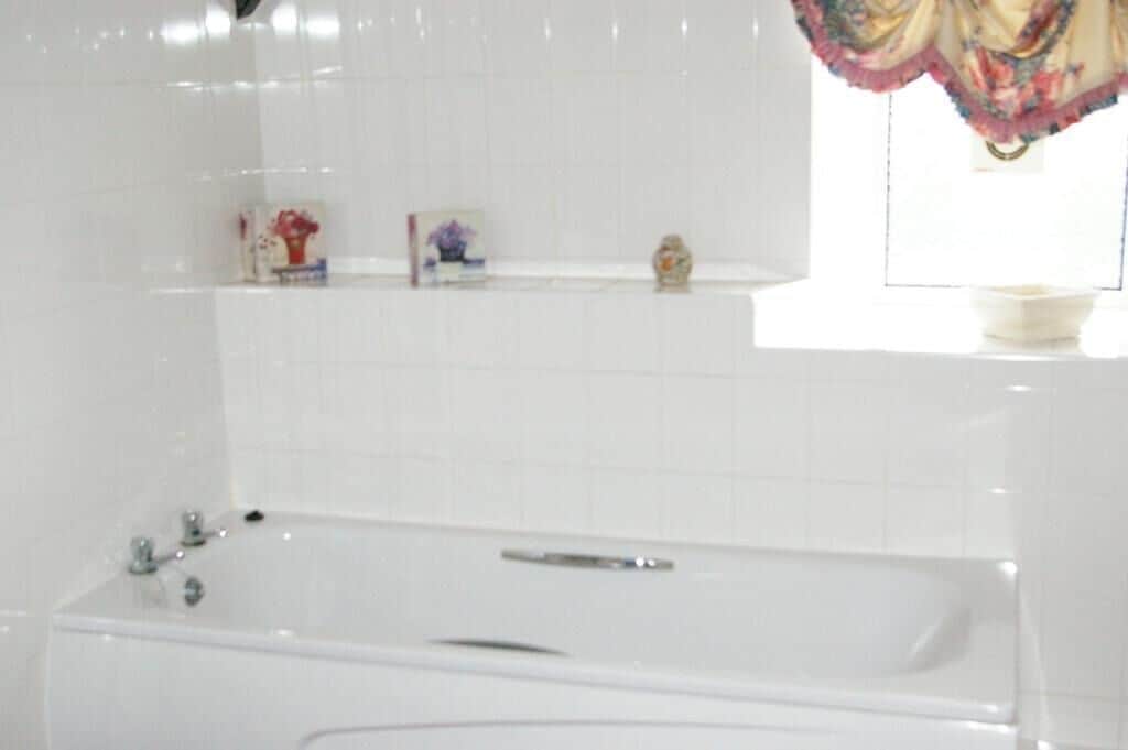 A bathroom with a white bathtub, a shelf with toiletries, and a window with a curtain.