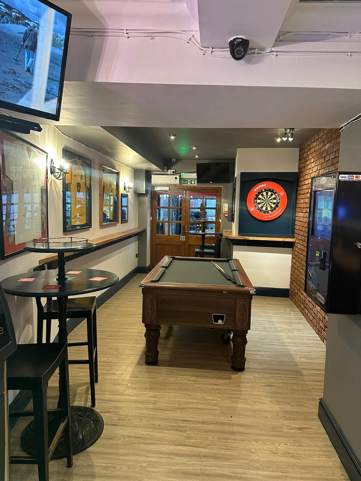 A billiards room with a pool table, a dartboard, and a television screen.