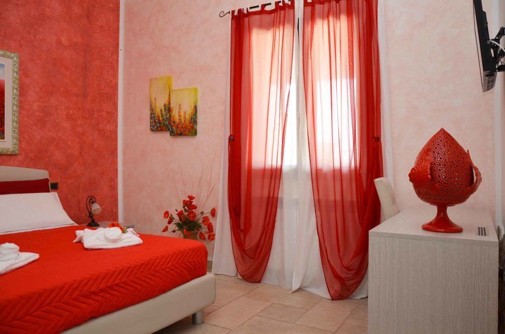 Ein Schlafzimmer mit roter Bettdecke, einem weißen Nachttisch und einem roten Dekorationsobjekt.