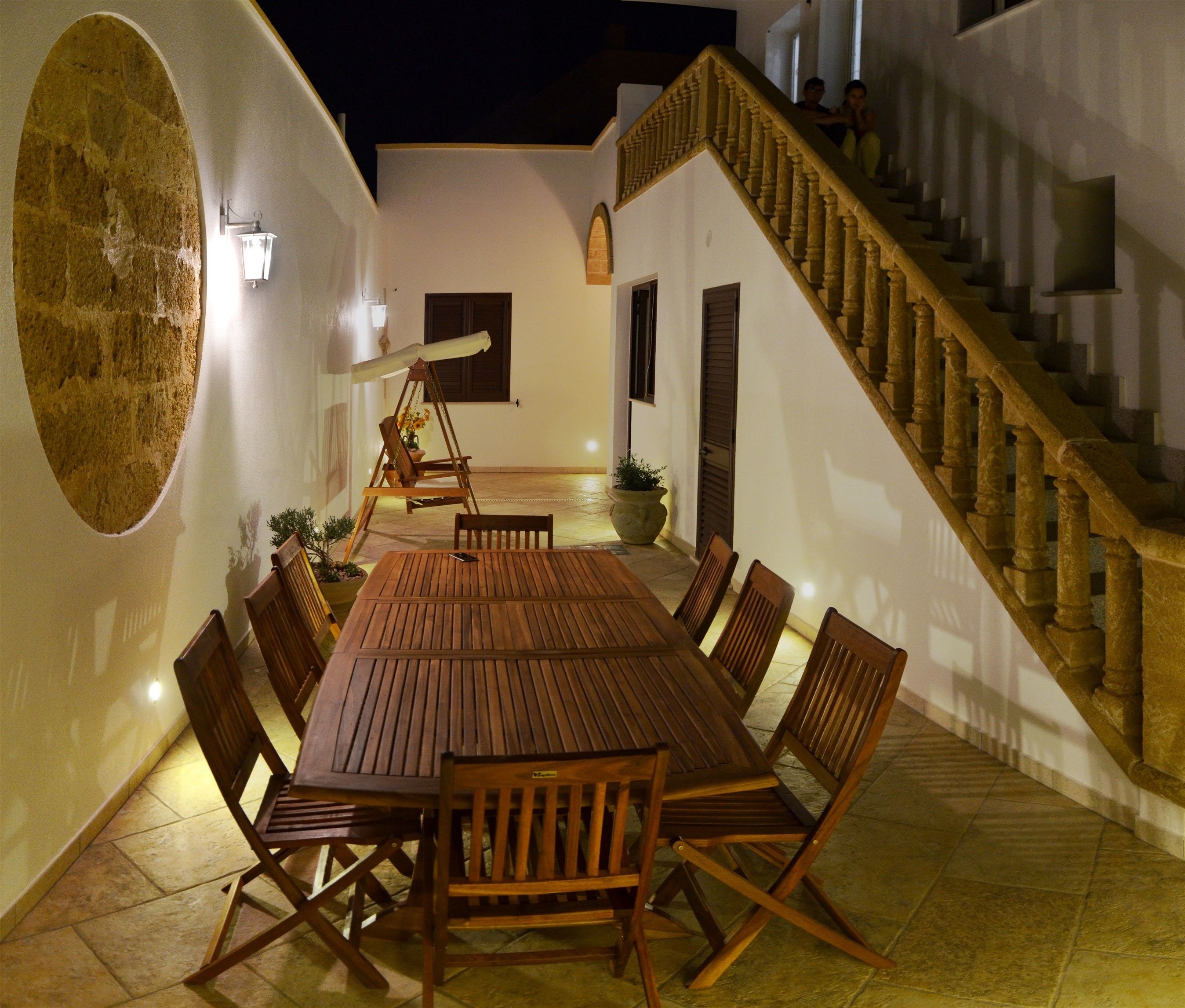 Un espacio exterior con comedor, una mesa y sillas de madera, un sillón columpio y una escalera.