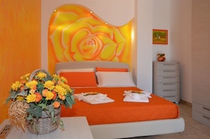 Quarto de hotel com uma cama, uma mesinha de cabeceira, uma cômoda e uma parede com design floral.