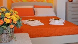 A hotel room with a large bed, orange bedding, a decorative rose mural on the wall, a wicker basket with flowers, and a small painting on the wall. - B&B Anemos (Morciano di Leuca)