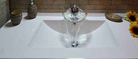 A bathroom sink with a modern faucet, a vase, and a decorative plate.