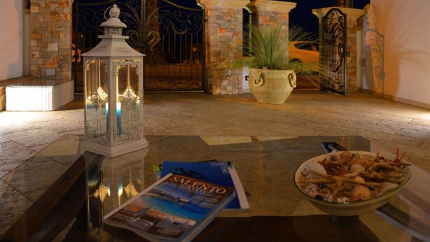 A table with a magazine, a bowl of seafood, and a lantern in a courtyard with stone walls and a gate. - B&B Anemos (Morciano di Leuca)