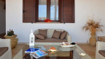 Un salón con una mesa de centro de cristal, un sofá de mimbre y una ventana con contraventanas.